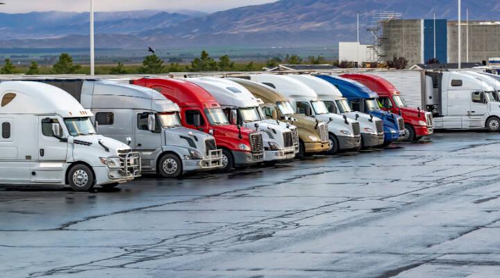 Row of semi-trucks parked side by side at a truck parking lot